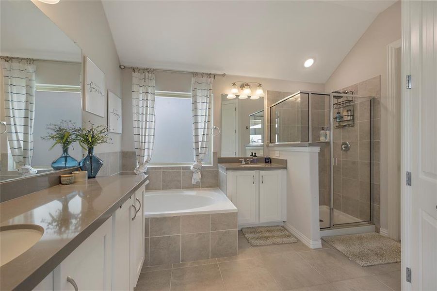 Bathroom featuring dual vanity, shower with separate bathtub, tile patterned flooring, and lofted ceiling