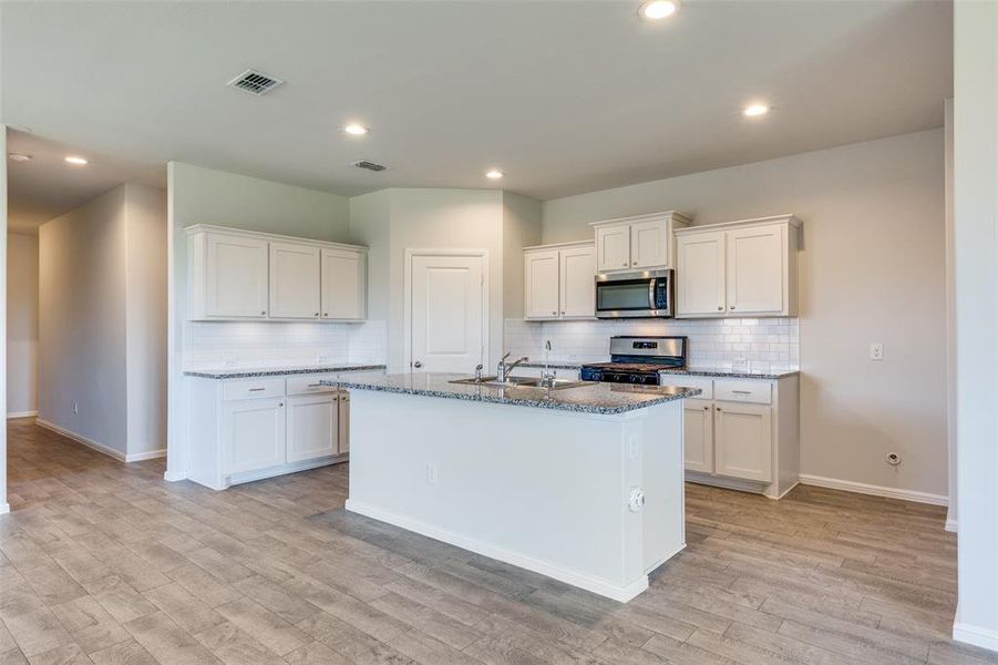 Kitchen featuring appliances with stainless steel finishes, a kitchen island with sink, white cabinetry, and light hardwood / wood-style flooring