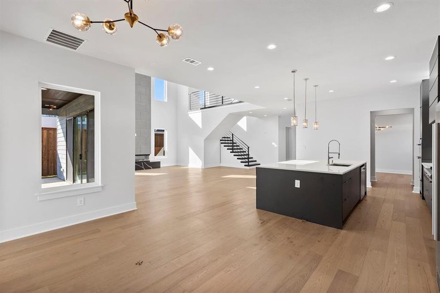 Kitchen with a kitchen island with sink, sink, hanging light fixtures, light hardwood / wood-style floors, and a chandelier