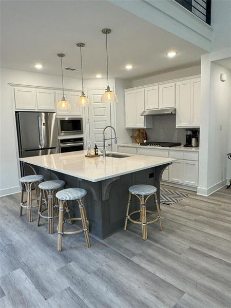 Kitchen featuring appliances with stainless steel finishes, sink, white cabinetry, and decorative light fixtures