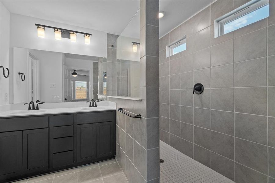 Bathroom with a tile shower, tile patterned flooring, a healthy amount of sunlight, and vanity