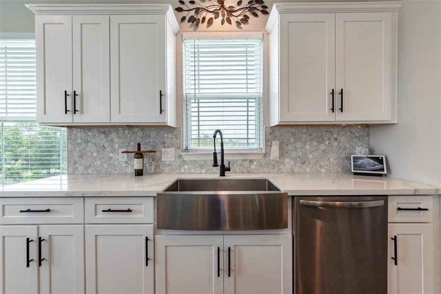 Oversized undermount stainless steel kitchen sink surrounded by marble backsplash and quartz countertops