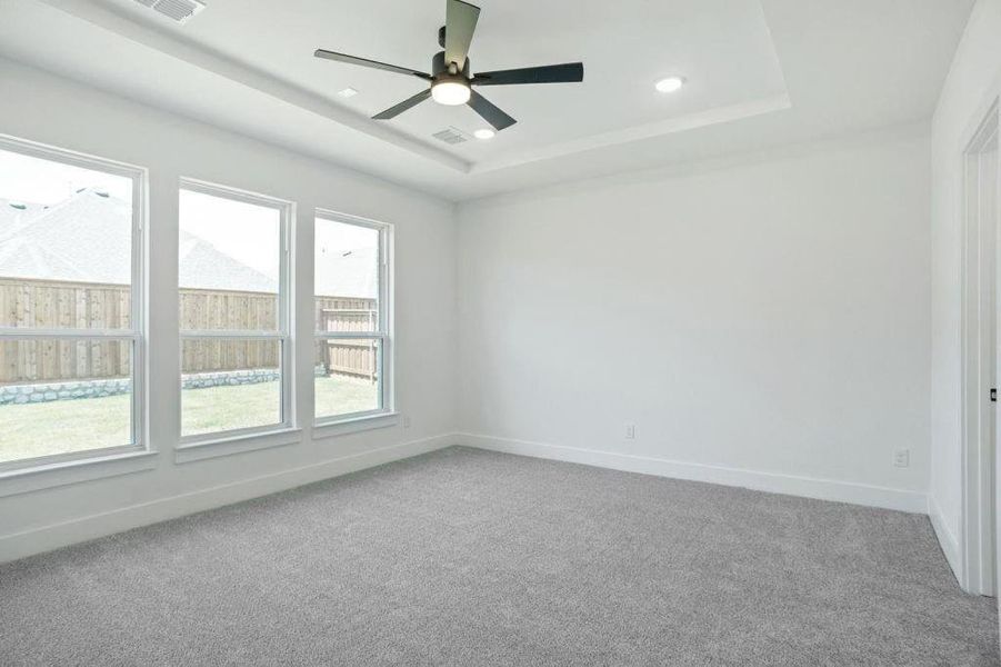 Carpeted empty room with ceiling fan and a raised ceiling