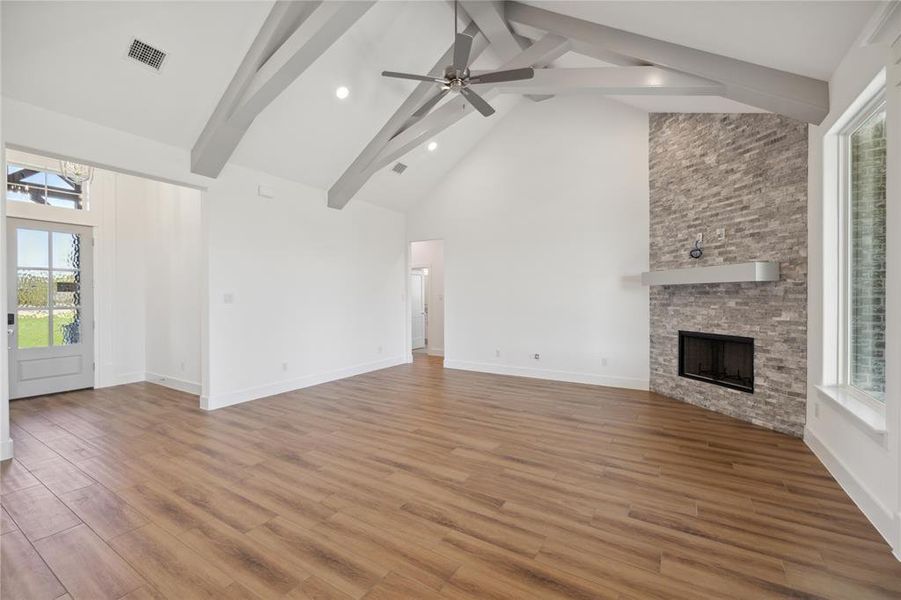 Unfurnished living room featuring a stone fireplace, plenty of natural light, beamed ceiling, and light hardwood / wood-style flooring