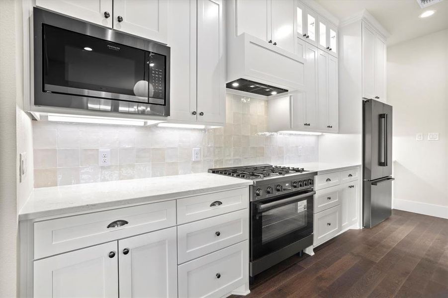 Kitchen with high end appliances, light stone countertops, decorative backsplash, dark wood-type flooring, and white cabinets