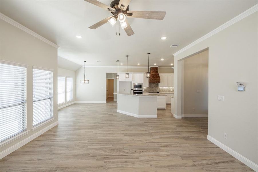 Kitchen featuring white cabinets, an island with sink, backsplash, custom range hood, and pendant lighting