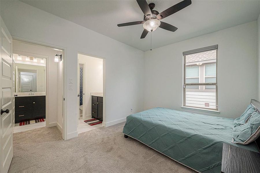This is a well-lit, cozy bedroom featuring a ceiling fan, plush carpeting, and direct access to an en suite bathroom. The neutral color palette offers a calming atmosphere.