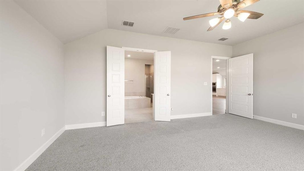 Unfurnished bedroom featuring connected bathroom, vaulted ceiling, carpet floors, and ceiling fan