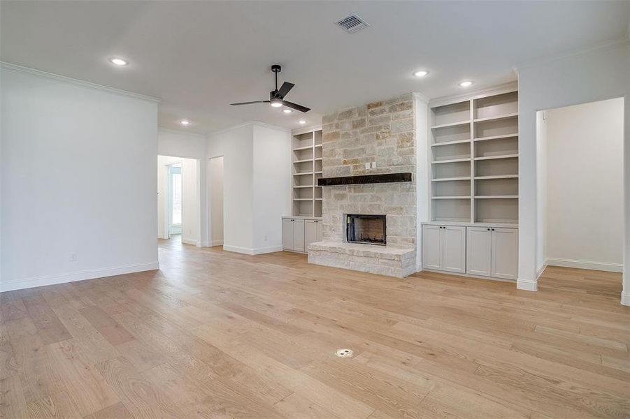 Unfurnished living room with a fireplace, ceiling fan, built in shelves, crown molding, and light wood-type flooring