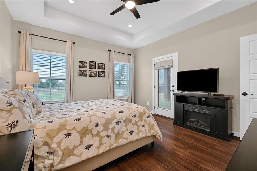 Bedroom featuring dark hardwood / wood-style flooring, access to exterior, a tray ceiling, and ceiling fan