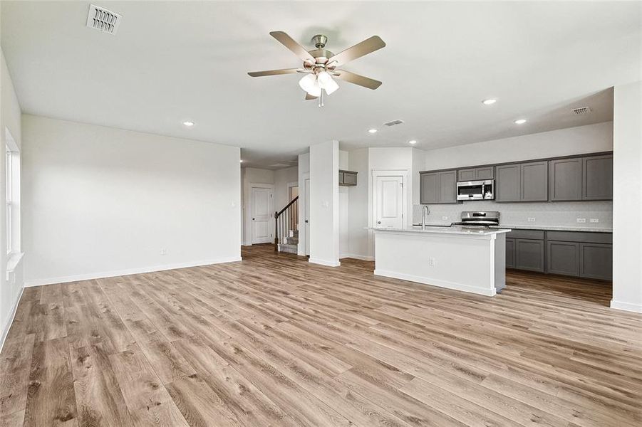 Kitchen with gray cabinetry, appliances with stainless steel finishes, light wood-type flooring, and a center island with sink