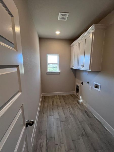 Laundry area featuring washer hookup, hookup for an electric dryer, light hardwood / wood-style flooring, hookup for a gas dryer, and cabinets