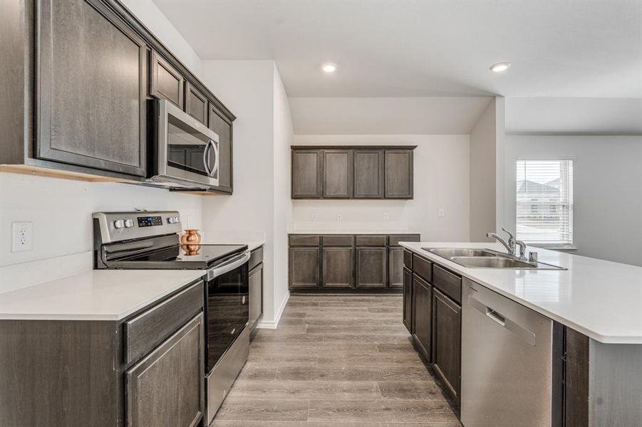 Kitchen with dark brown cabinets, sink, stainless steel appliances, and light hardwood / wood-style floors