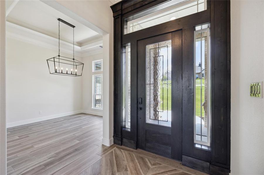 Foyer with a raised ceiling, light hardwood / wood-style flooring, and a notable chandelier