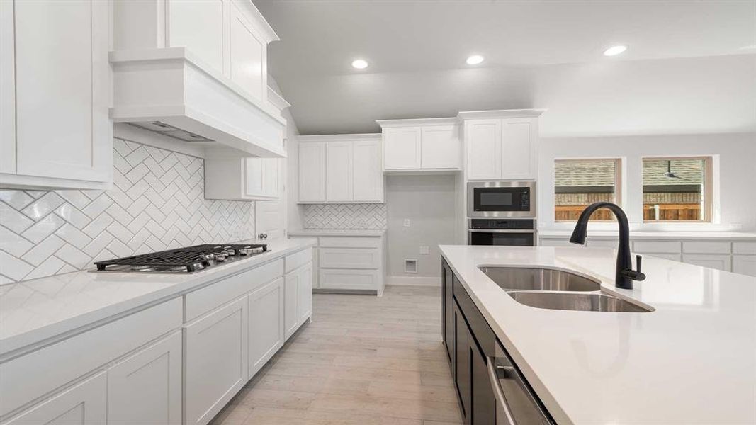 Kitchen with white cabinets, light hardwood / wood-style floors, appliances with stainless steel finishes, decorative backsplash, and sink