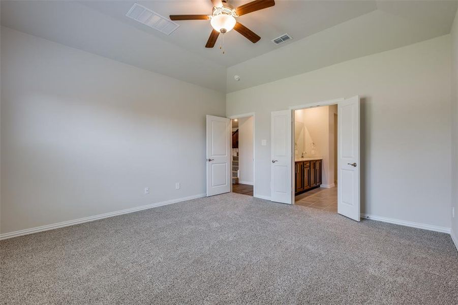 Unfurnished bedroom with light carpet, ensuite bathroom, ceiling fan, and high vaulted ceiling
