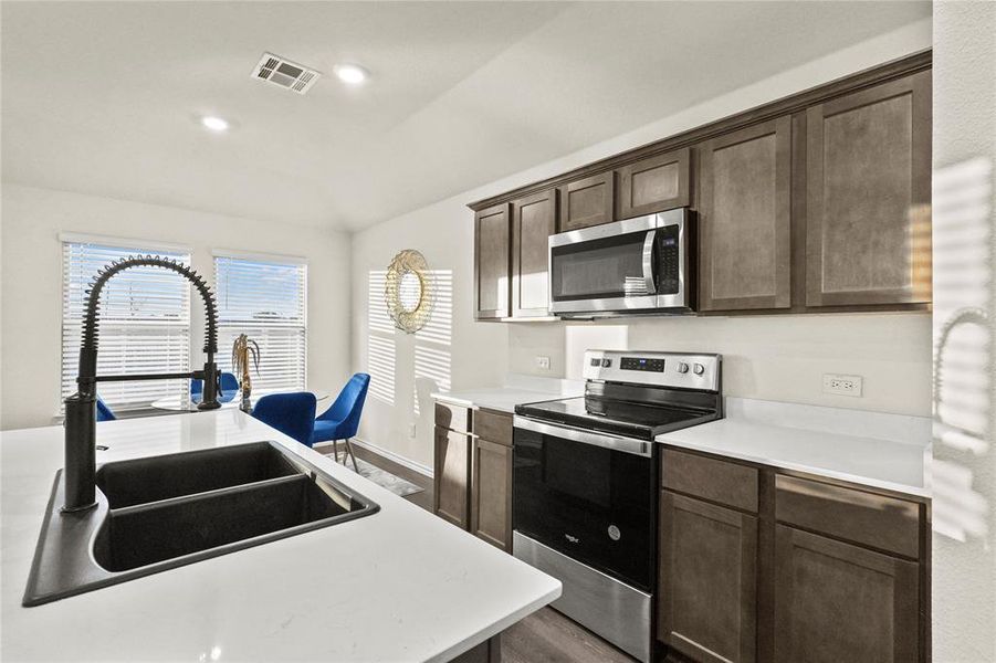 Kitchen featuring appliances with stainless steel finishes, vaulted ceiling, dark brown cabinets, hardwood / wood-style floors, and sink