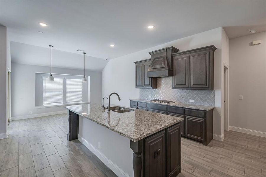 Kitchen featuring light stone counters, an island with sink, light wood-type flooring, custom range hood, and sink