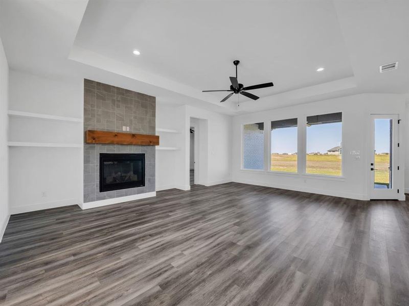 Unfurnished living room with dark wood-type flooring, a raised ceiling, a tiled fireplace, and ceiling fan