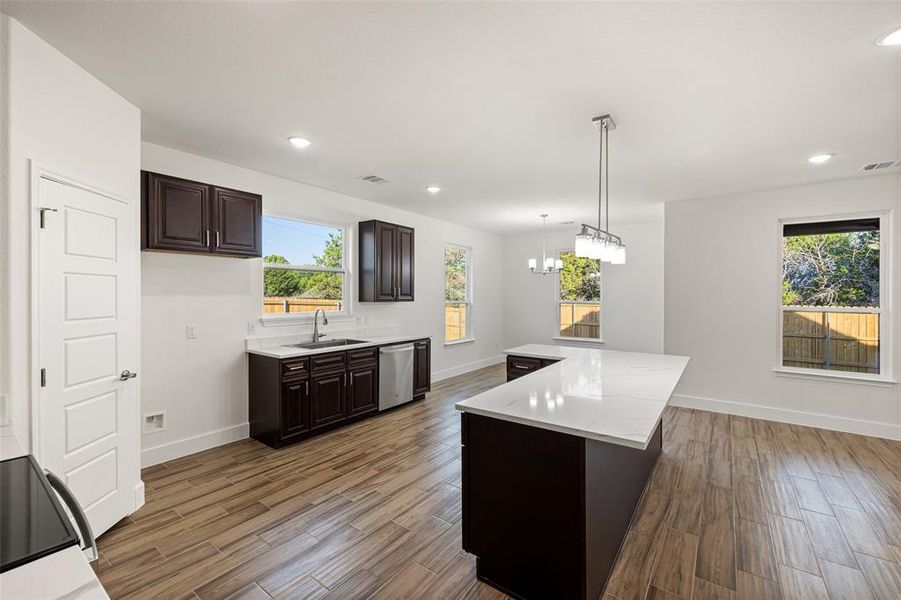 Kitchen featuring hanging light fixtures, plenty of natural light, dark wood-type flooring, dishwasher, and a center island