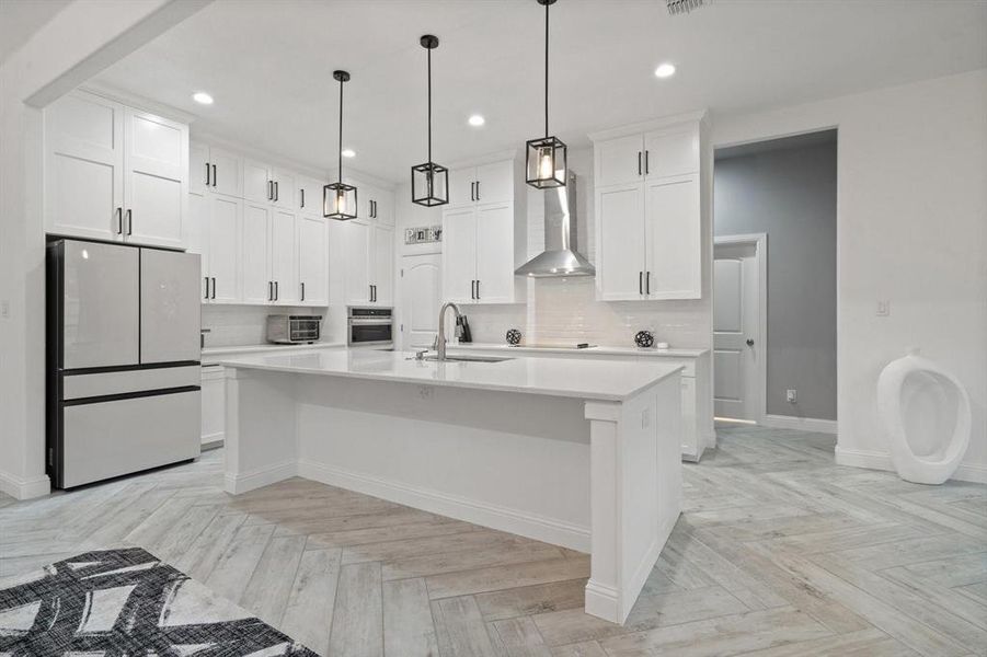 Kitchen with wall chimney exhaust hood, white fridge, oven, a center island with sink, and sink