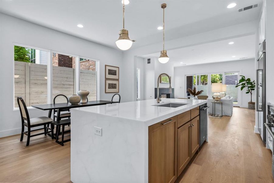 Kitchen with an island with sink, pendant lighting, light wood-type flooring, and plenty of natural light