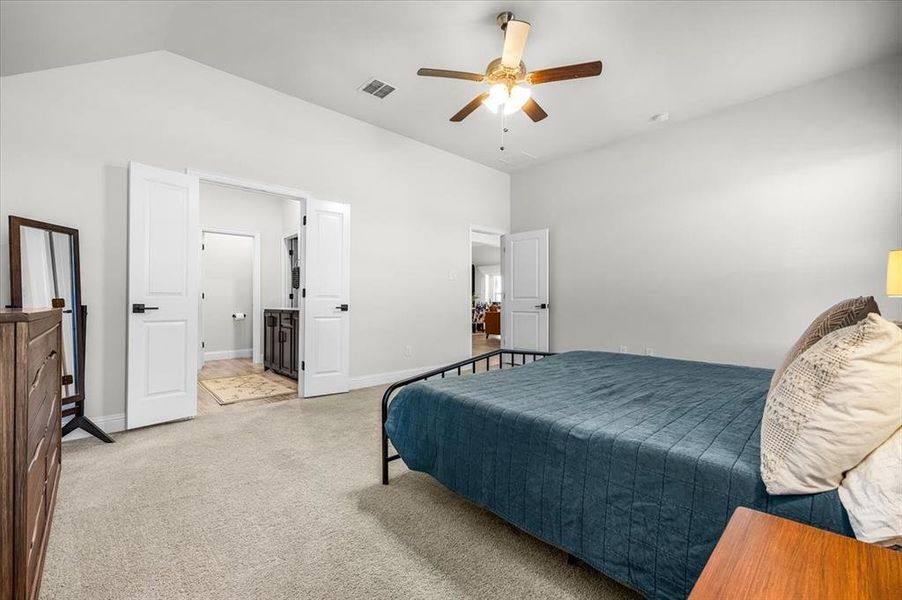 Bedroom featuring ensuite bath, ceiling fan, light colored carpet, and vaulted ceiling