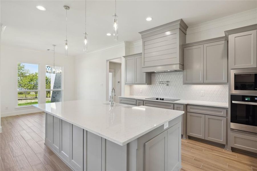 Kitchen with sink, pendant lighting, custom range hood, and light hardwood / wood-style floors