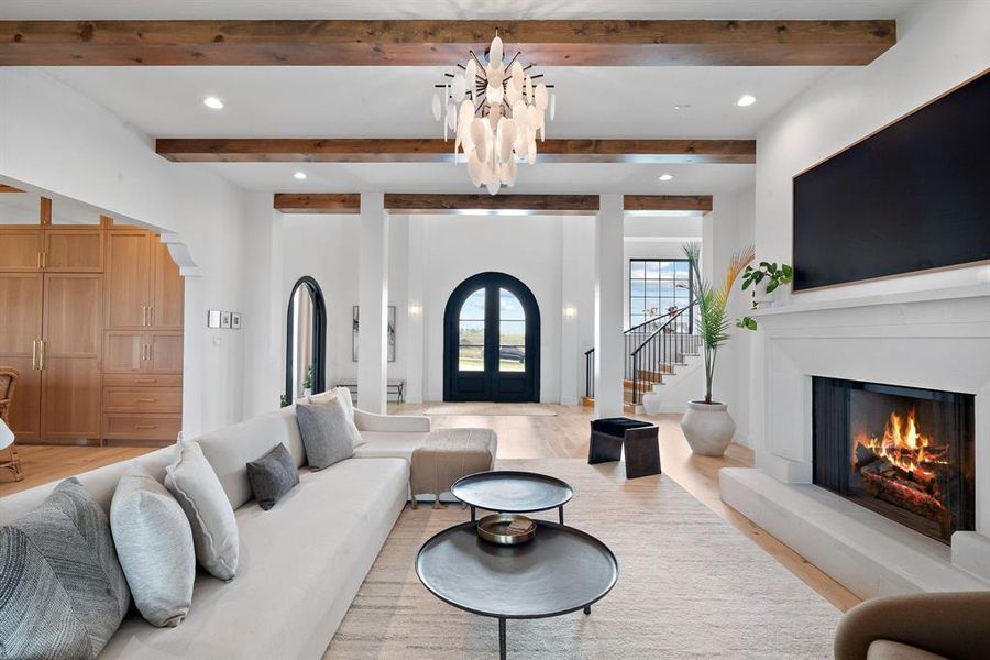 Living room with beam ceiling, light hardwood / wood-style floors, and a notable chandelier