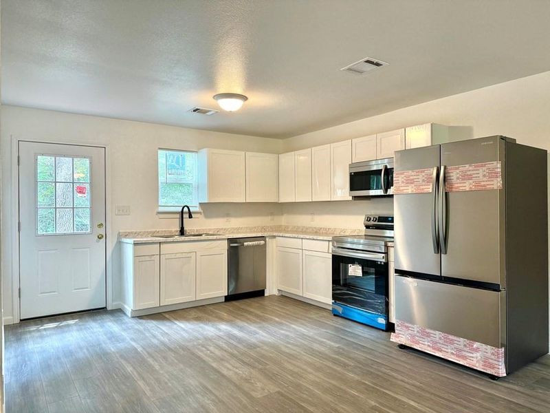 Kitchen with sink, white cabinets, light wood-type flooring, and stainless steel appliances