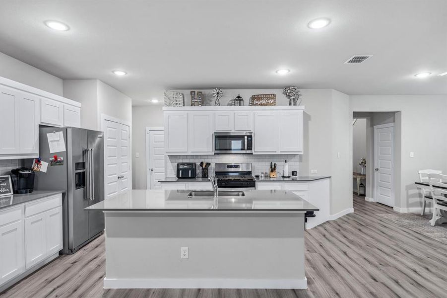 Kitchen with light hardwood / wood-style floors, backsplash, a kitchen island with sink, white cabinetry, and appliances with stainless steel finishes