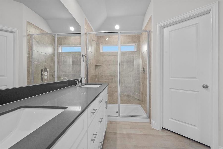 Bathroom featuring a shower with shower door, wood-type flooring, lofted ceiling, and double vanity