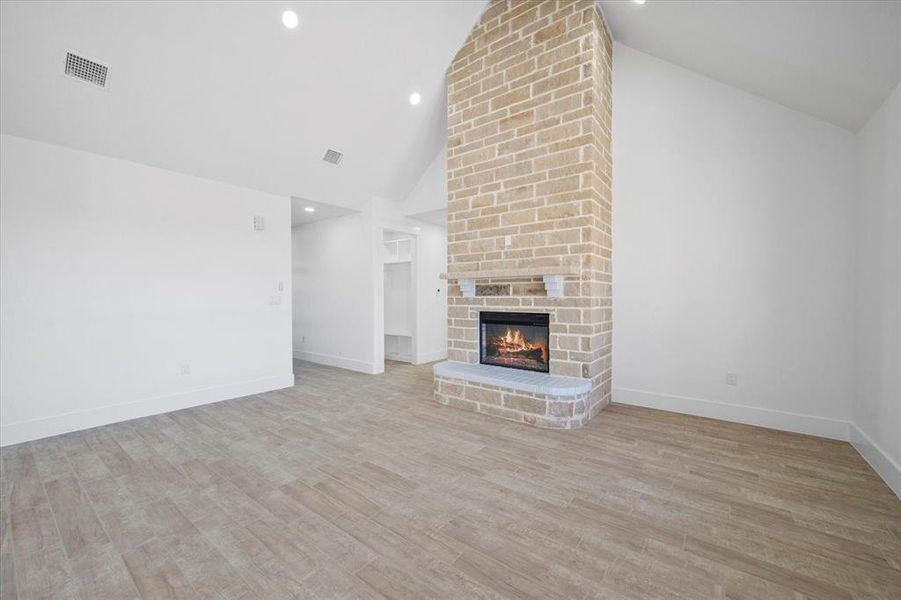 Unfurnished living room with high vaulted ceiling, brick wall, light wood-type flooring, and a brick fireplace