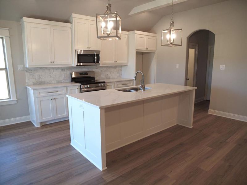 Kitchen with appliances with stainless steel finishes, hanging light fixtures, white cabinets, a center island with sink, and sink