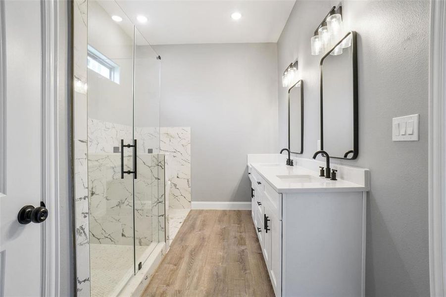 Bathroom with dual vanity, a shower with shower door, and hardwood / wood-style flooring