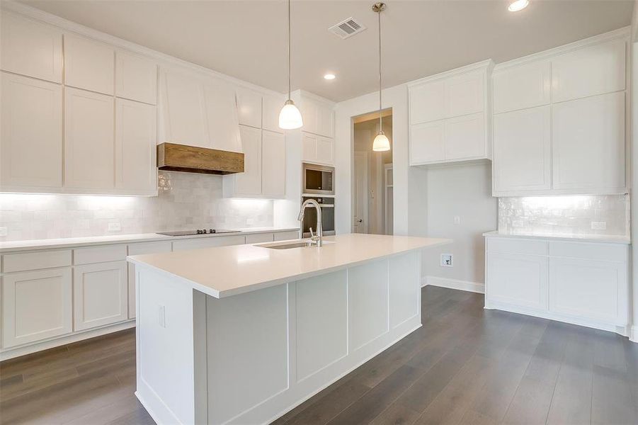 Kitchen featuring sink, dark hardwood / wood-style flooring, decorative backsplash, and an island with sink