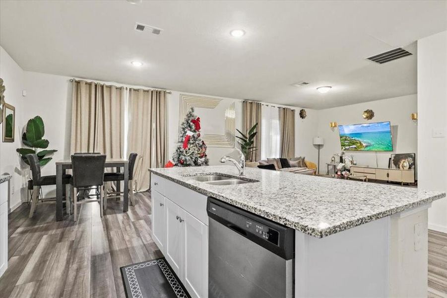 Kitchen with stainless steel dishwasher, sink, wood-type flooring, a center island with sink, and white cabinets