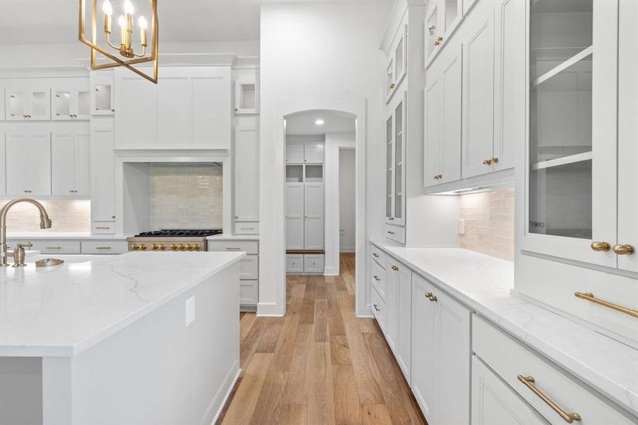 Kitchen featuring light stone counters, pendant lighting, white cabinets, backsplash, and light wood-type flooring