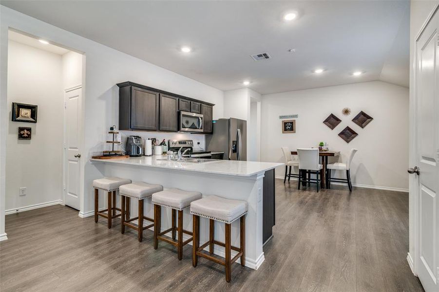 Kitchen with dark brown cabinetry, kitchen peninsula, appliances with stainless steel finishes, a breakfast bar area, and light hardwood / wood-style floors