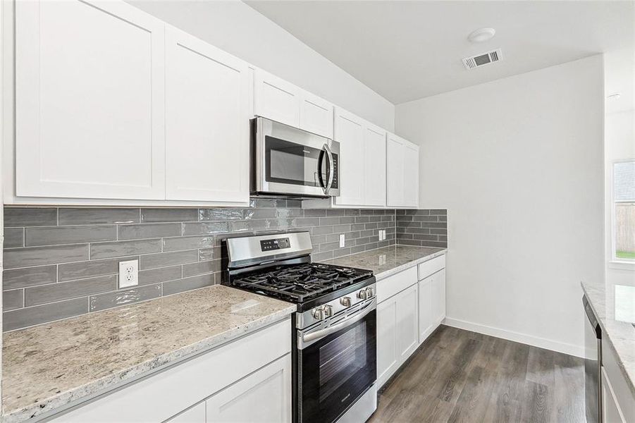 Kitchen featuring light stone counters, dark hardwood / wood-style floors, tasteful backsplash, and stainless steel appliances