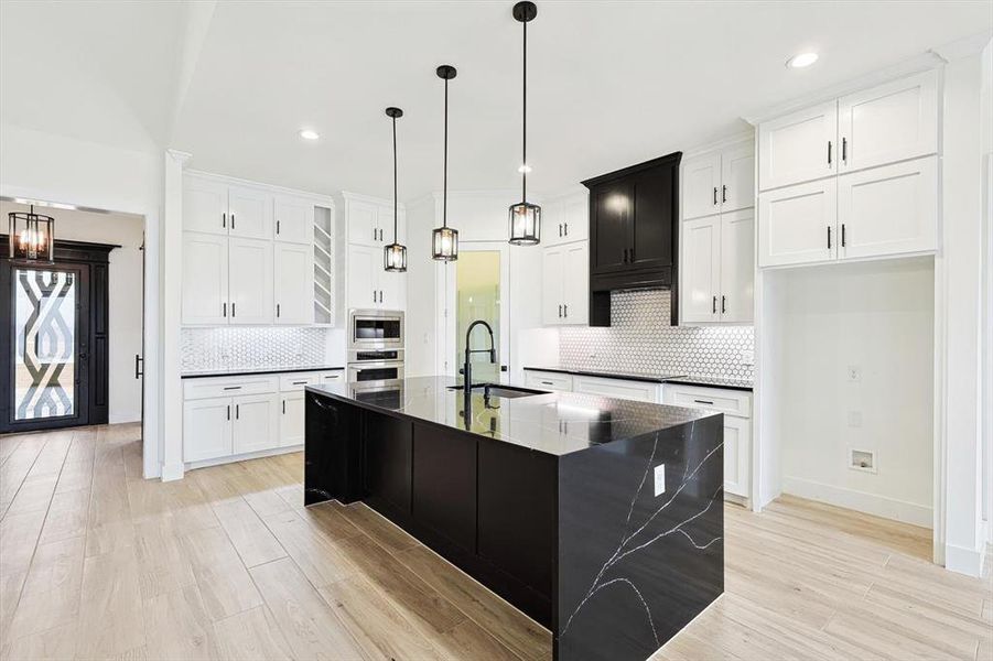 Kitchen featuring appliances with stainless steel finishes, tasteful backsplash, dark stone counters, a center island with sink, and sink