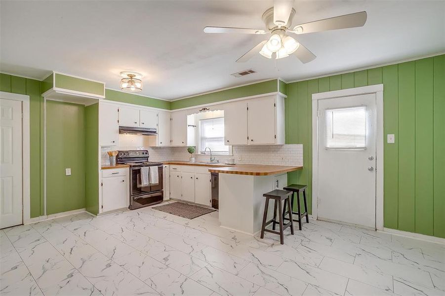 Kitchen with black electric range oven, white cabinets, a kitchen bar, and kitchen peninsula