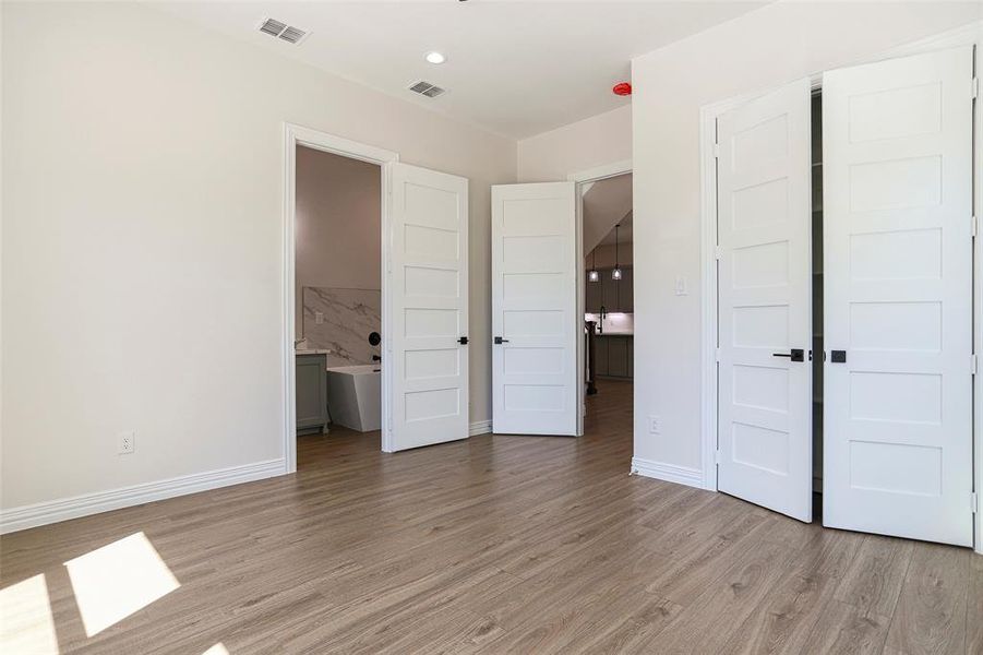 Unfurnished bedroom with ensuite bathroom and light hardwood / wood-style floors