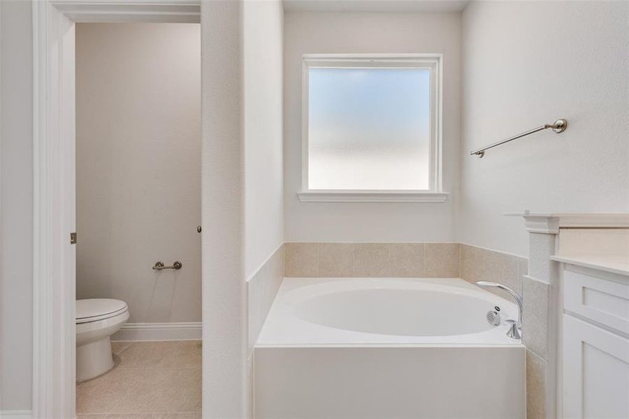 Bathroom featuring vanity, a tub to relax in, tile patterned flooring, and toilet