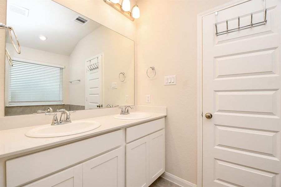 This is a bright, clean bathroom featuring a large vanity with dual sinks, ample counter space, and storage. It also has a privacy window providing natural light.