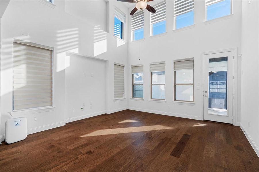 Unfurnished living room with dark wood-type flooring, a towering ceiling, and ceiling fan