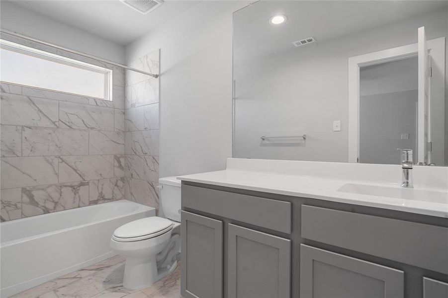 Secondary bath features tile flooring, bath/shower combo with tile surround, stained cabinets, beautiful light countertops, mirror, sleek fixtures and modern finishes.