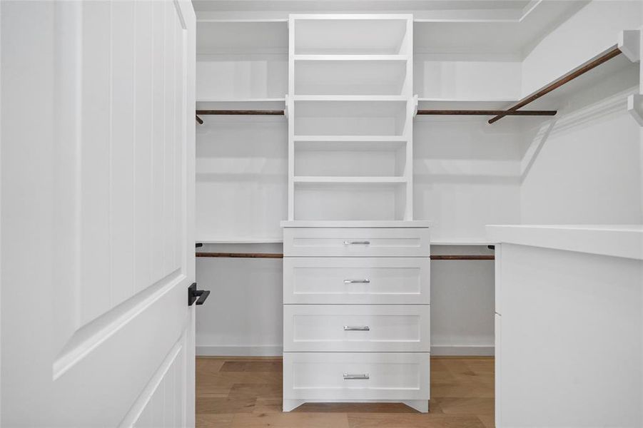 Spacious walk-in closet with built-in white drawers and ample shelving, featuring a combination of hanging space and storage options for organization.