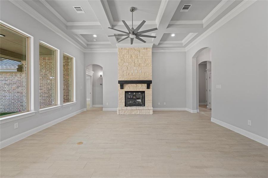 Unfurnished living room with coffered ceiling, a stone fireplace, beamed ceiling, ornamental molding, and ceiling fan