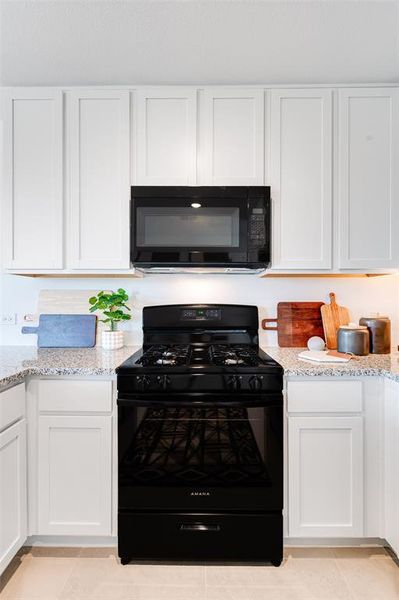 Kitchen featuring white cabinetry, black appliances, light tile patterned floors, and light stone countertops